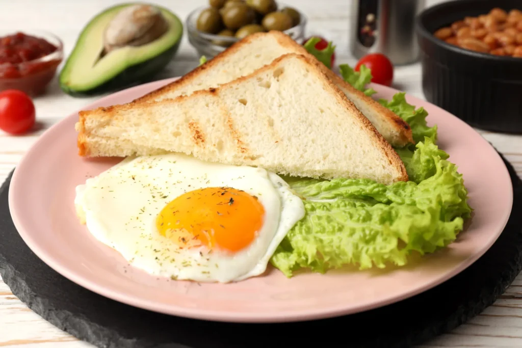 Sunny-side-up egg with toast, avocado, lettuce, olives, and cherry tomato on rustic wooden table.